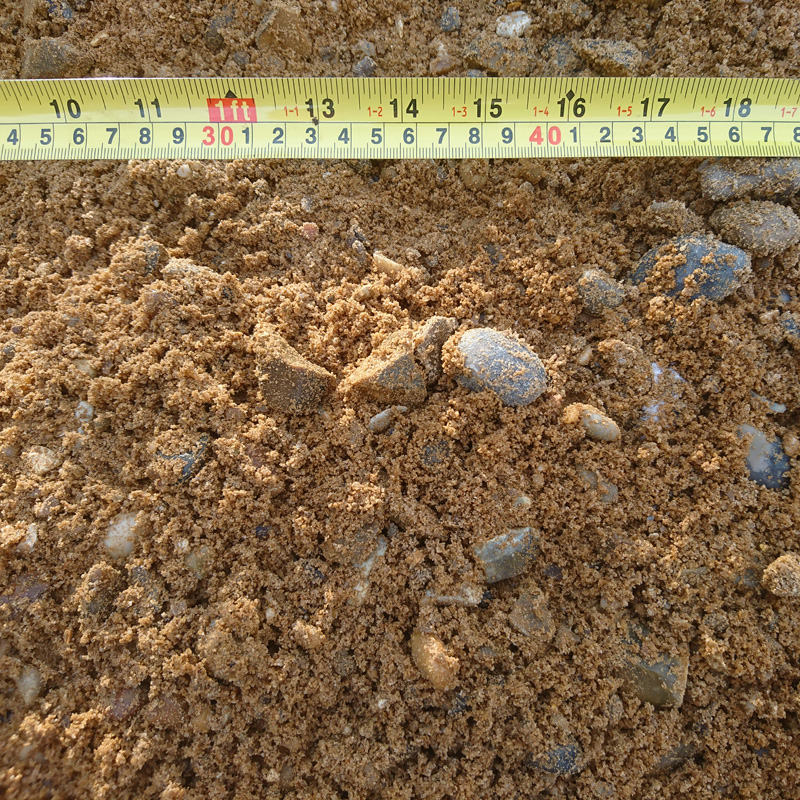 A close-up shows bagged coarse sand with small stones, named Ballast 20mm - Bagged. A measuring tape in centimeters, ranging from 0 to 35, highlights the varied texture and size of this vital construction material.