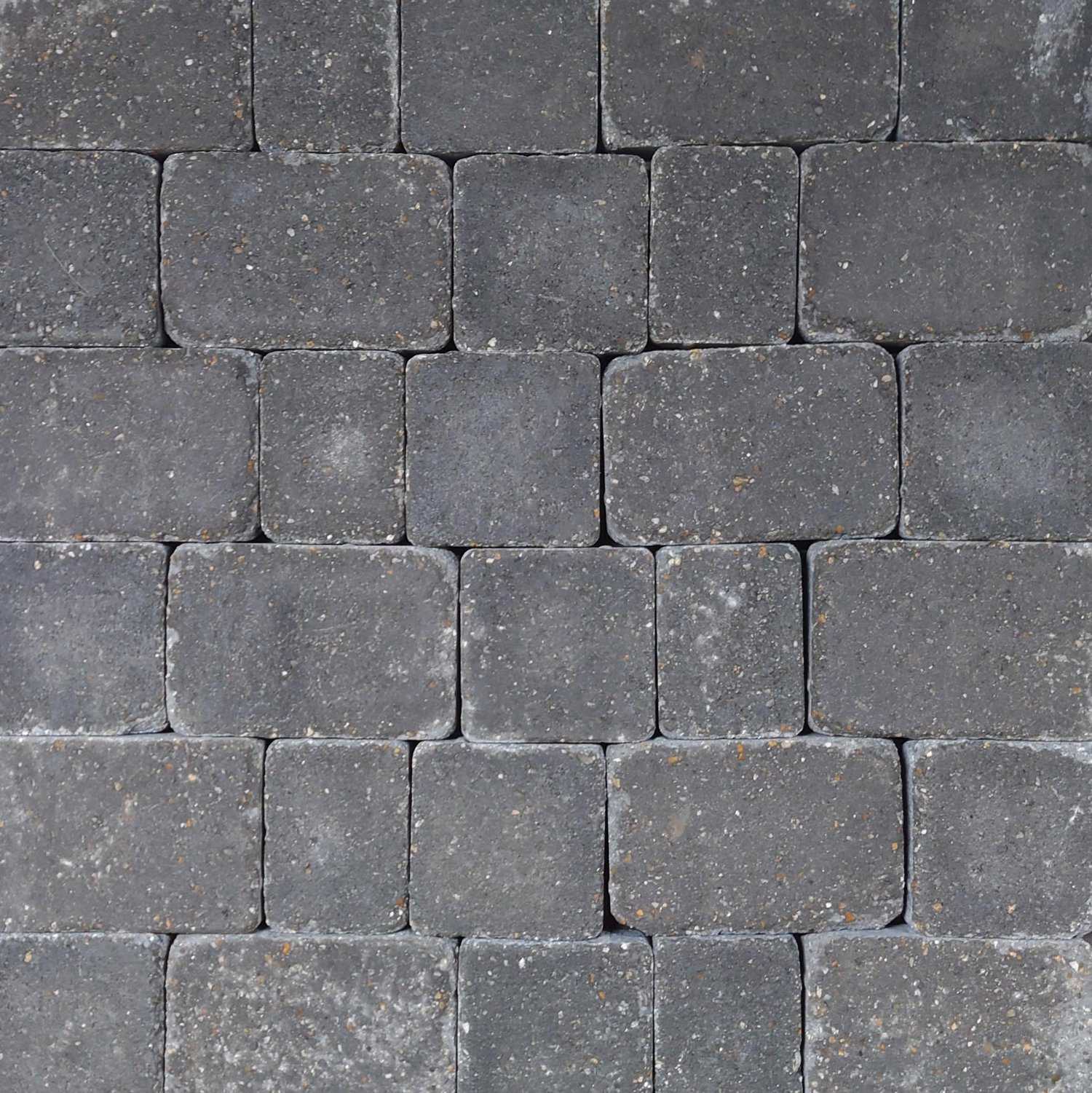 Close-up of neatly arranged rectangular Breedon 50mm Norfolk Rumbled Charcoal Setts with a slightly rough, speckled surface. They're laid in an interlocking pattern for a uniform look, beautifully captured through a 50mm lens.