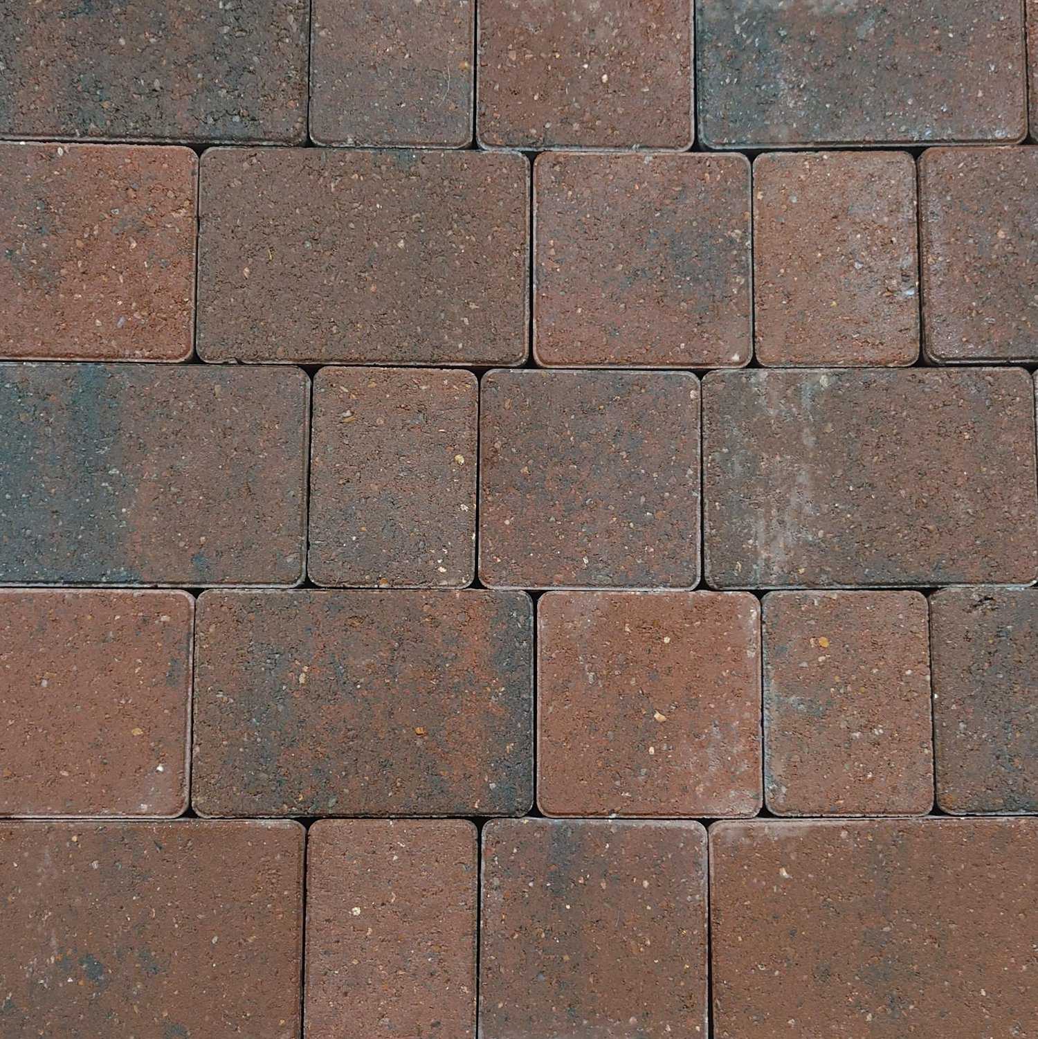 A close-up of Breedon 50mm Suffolk Smooth Burnt Ochre Setts reveals rectangular bricks in a woven pattern, featuring various brown, red, and burnt ochre shades, with darker patches suggesting weathering or use.