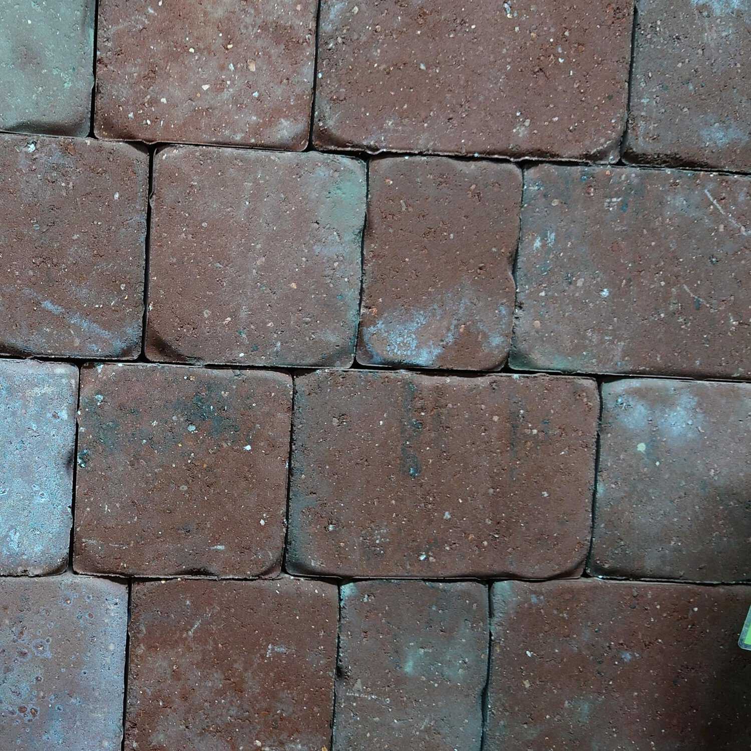 A stack of Cemex 50mm ReadyPave CAMDEN Burnt Ember rectangular bricks is neatly arranged in a grid. Some bricks have gray and white speckles, indicating wear. The texture is rough, with slight color variation among the bricks.