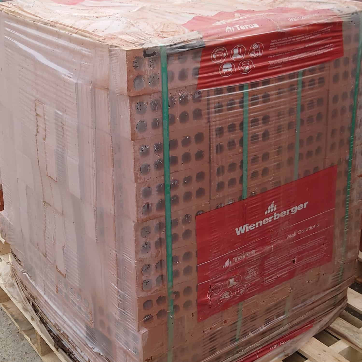 A pallet loaded with 65mm Wienerberger Multi Guilt Stock Bricks is wrapped in clear plastic and secured with green straps. The Wienerberger branding is prominently displayed, and the sturdy wooden base ensures stability during transport.