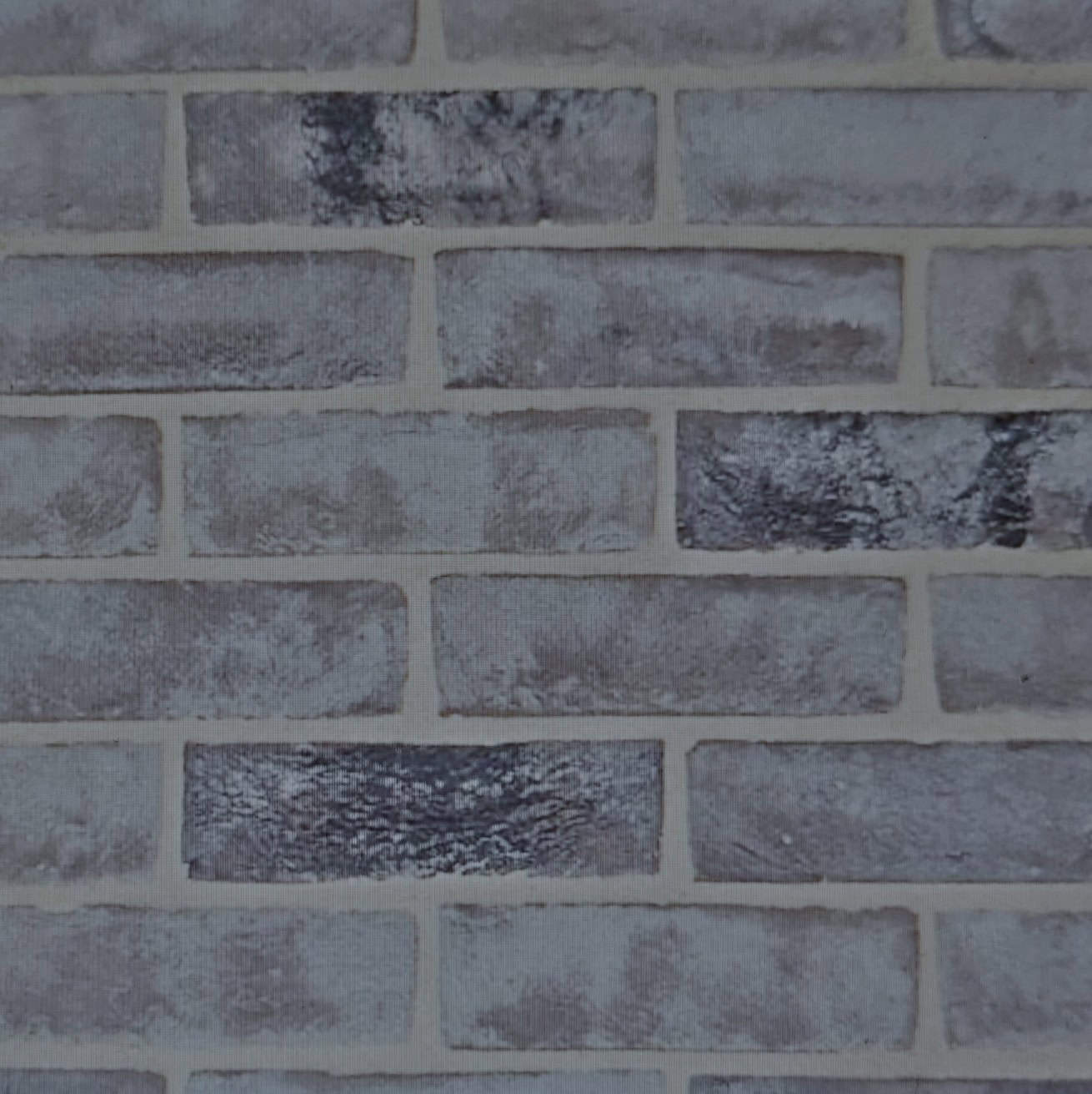 The image depicts a gray brick wall with a weathered texture, showcasing Wienerberger PAGUS BLACK GREY 65mm bricks. These bricks are laid horizontally, displaying nuanced shading and color variations that enhance the rustic look.