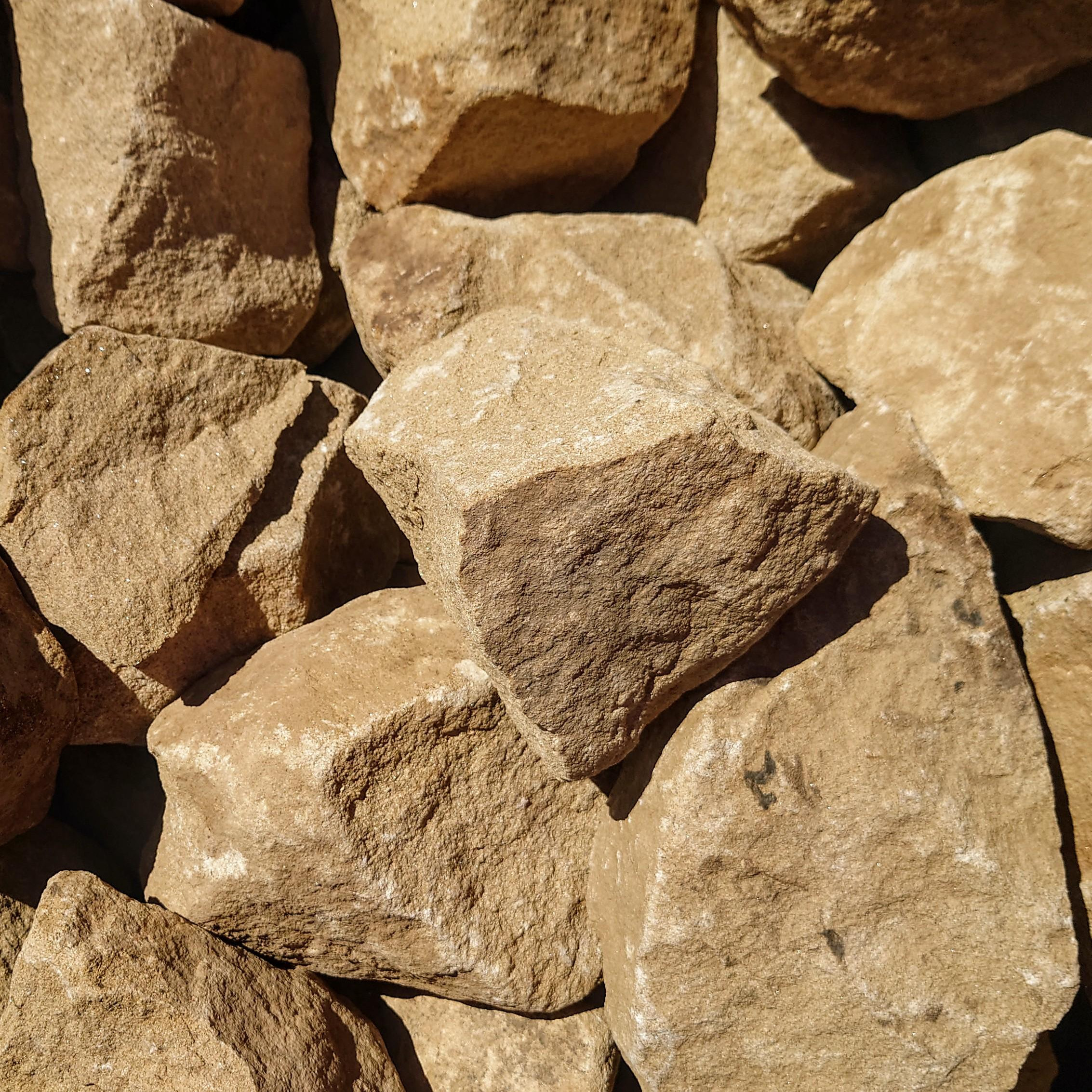 A close-up shows sunlit 300-400mm Cotswold Rockery stones, highlighting their rough texture and uneven surfaces.