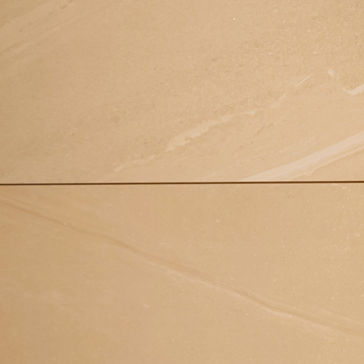 Close-up of a Nuova Beige Porcelain 900x600x20mm tile surface showing subtle veining and a horizontal seam, dividing it slightly into two sections. Its smooth, polished texture closely resembles elegant beige marble.