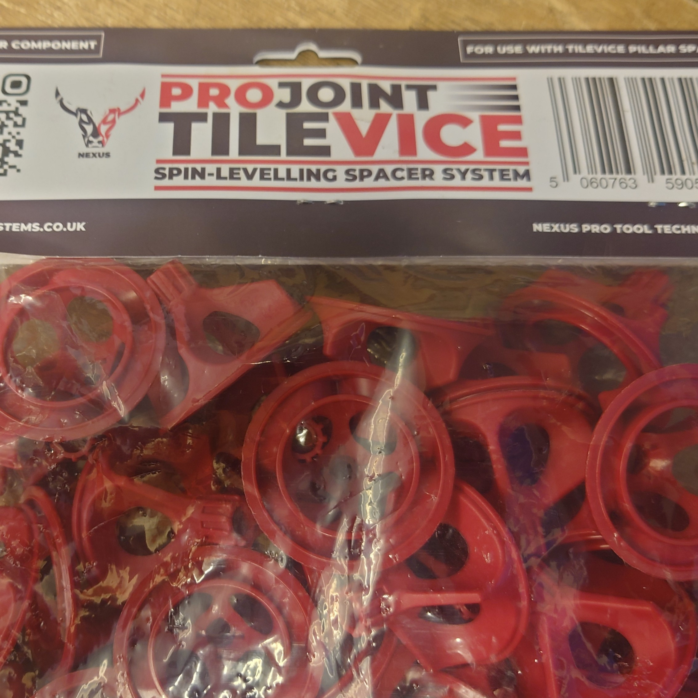 Close-up of a red ProJoint Porcelain Tile Vice Spinner package for porcelain tiles. The transparent bottom shows the red spacers, while the top displays branding and a QR code, emphasizing its innovative Vice Spinner technology.